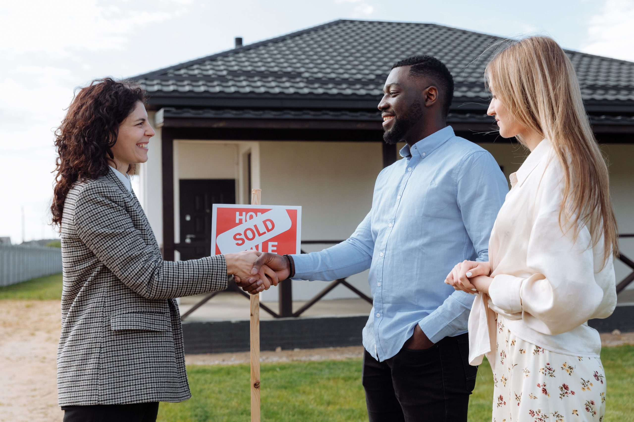 Real estate agent sealing a deal with a diverse couple in front of their new house.